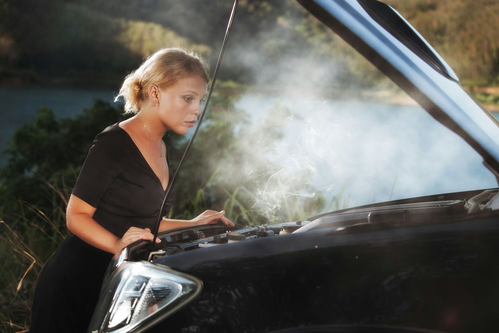 A woman looking under the hood of her car with a smoking AC.