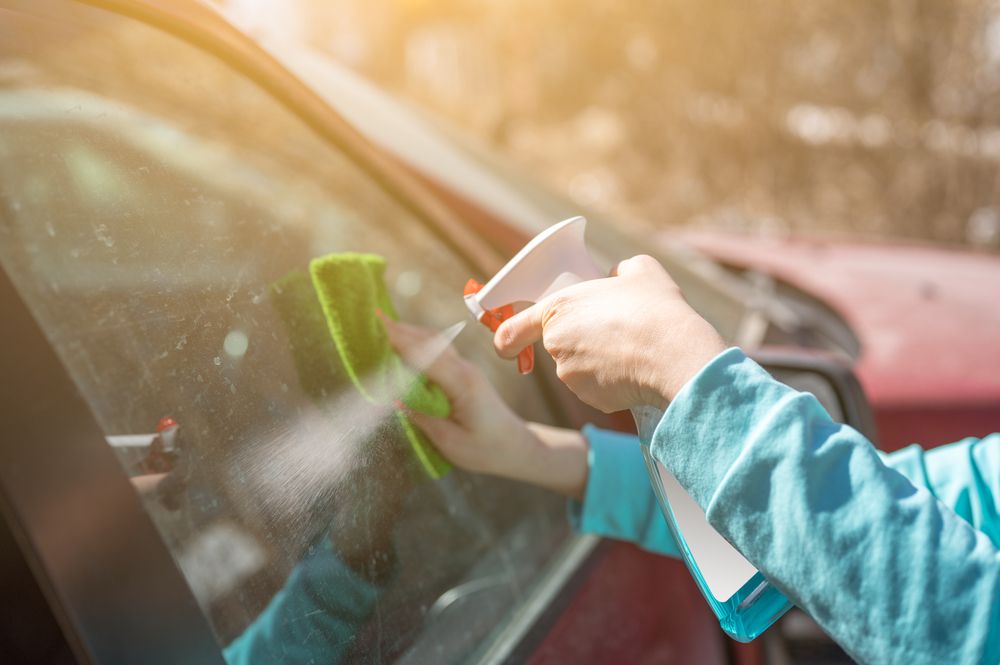 Cleaning a car window with windex.