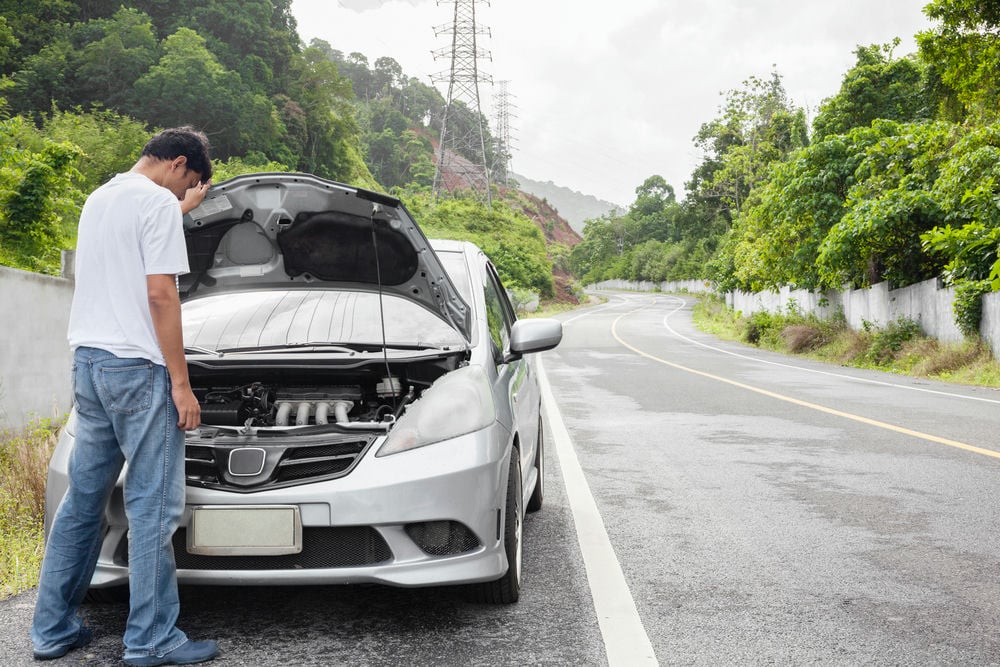 A man looking over an engine that has failed due to catastrophic damage from driving while it is overheating.