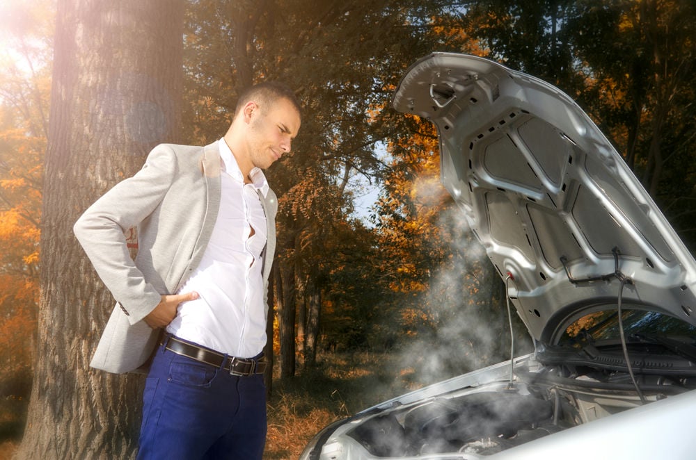 A man looking over his overheating engine on the side of the road.