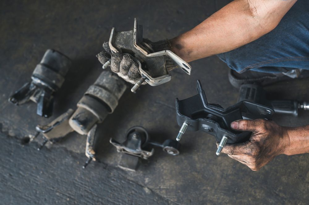 A mechanic comparing a new versus old motor mount.