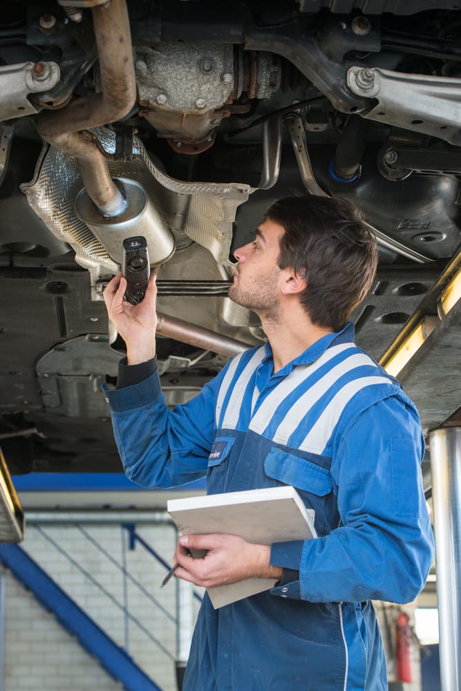 A mechanic inspecting a recently installed muffler for any leaks.