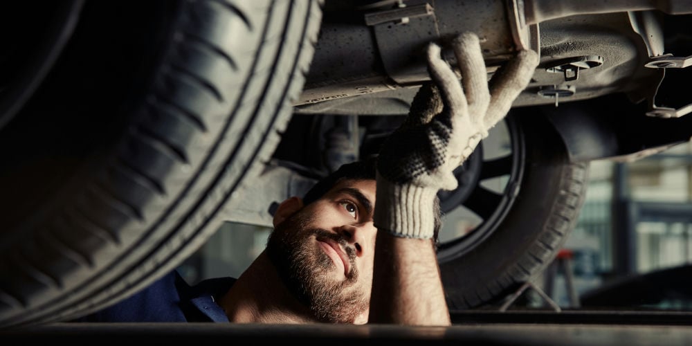 A mechanic inspecting a muffler for exhaust leaks.