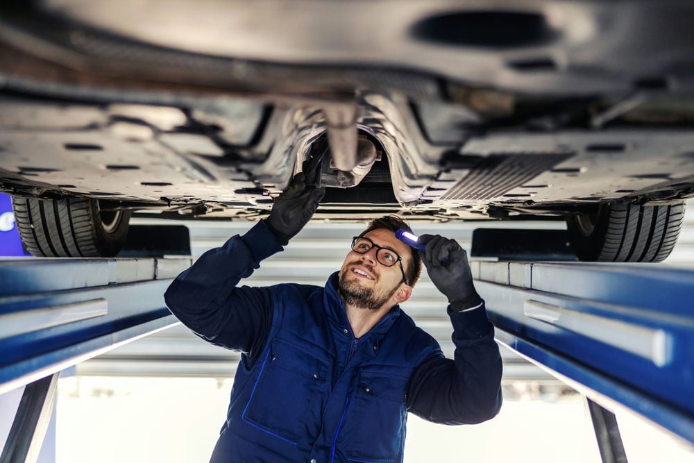 A mechanic looking for an exhaust leak under a car.