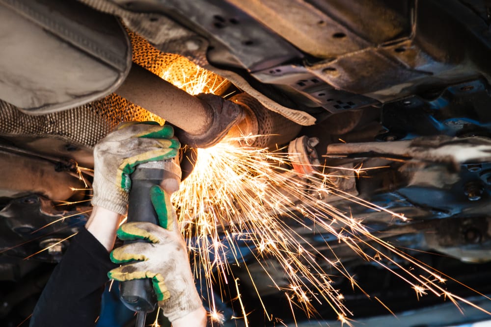 A mechanic removing a muffler to straight pipe a car.