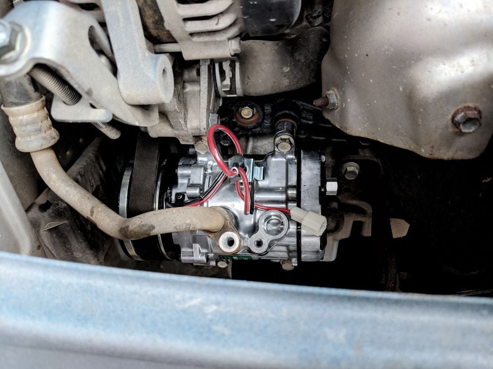 A recently installed AC compressor in a car.