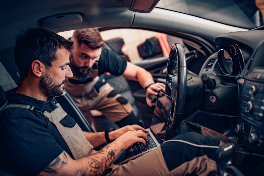 Two mechanics tuning a car with a laptop on a dyno.