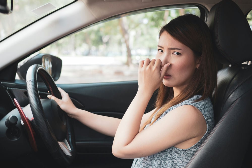 A woman smelling what smells like sulphur in her car cabin.